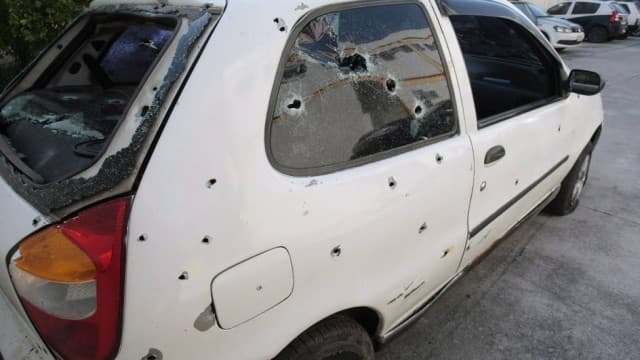 Carro branco crivado de tiros, com vidros estilhaçados, após entrar em área de risco no Rio de Janeiro